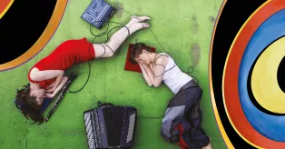 Två musiker som ligger på golvet vid sina instrument. Foto.